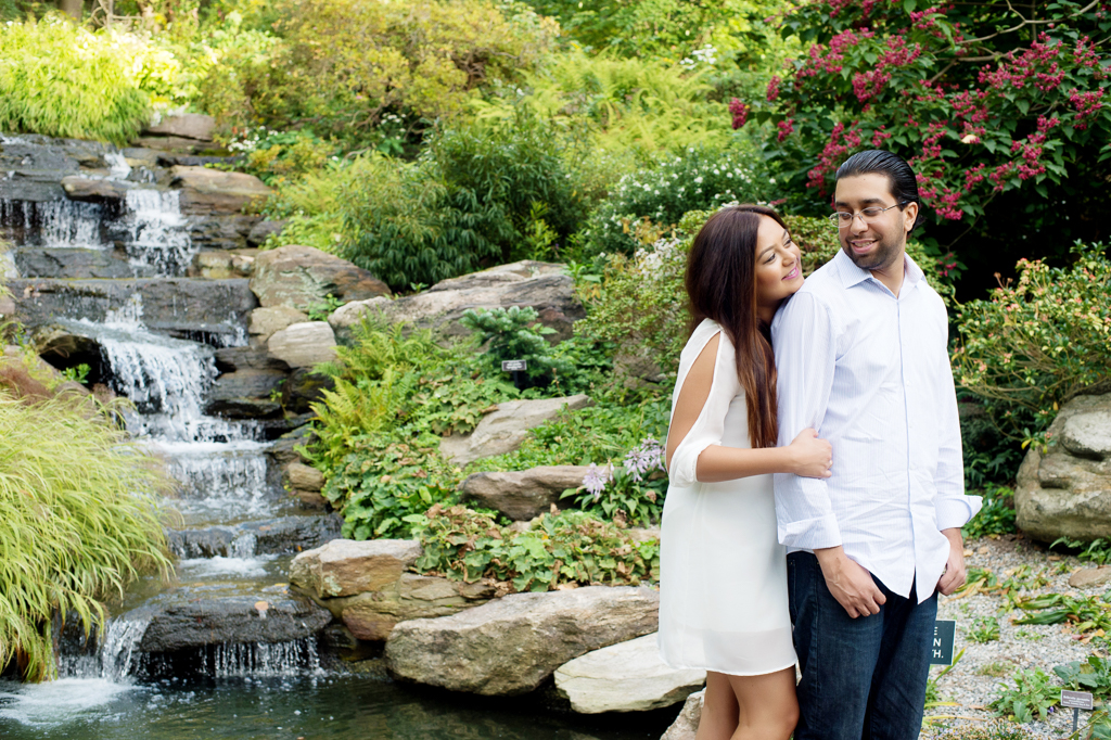 a couple laughs in front of a waterfall at new york botanical garden