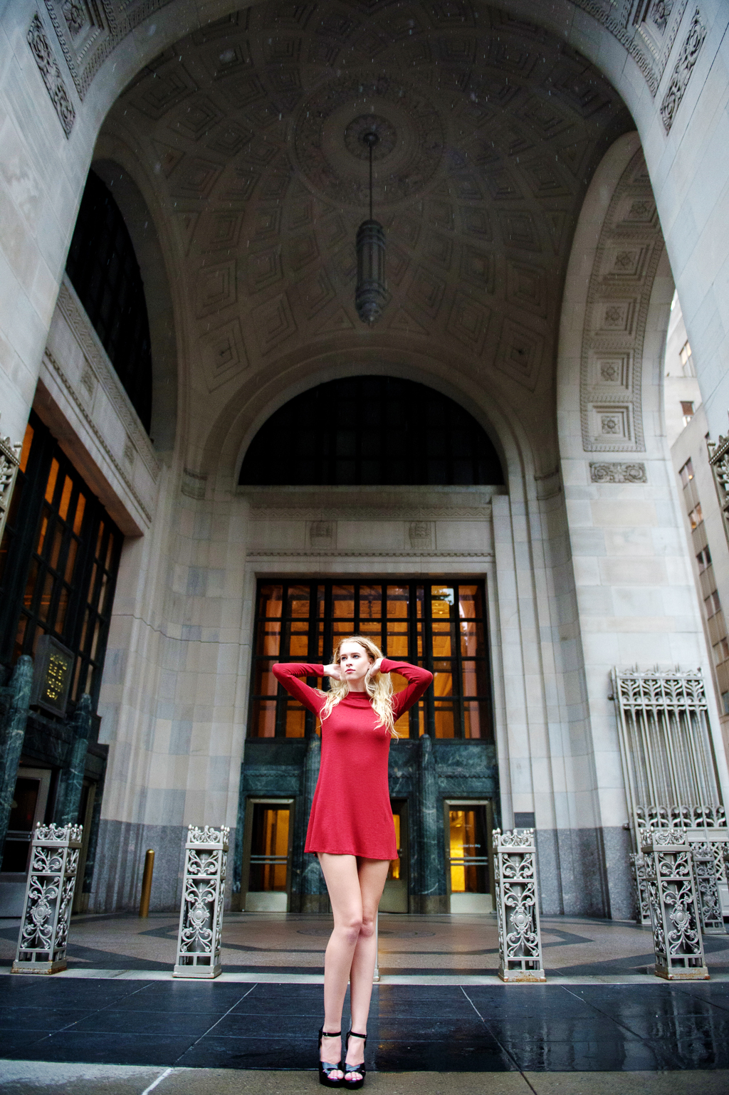 a model in a red dress with long blonde hair stands in front of a very old building in nyc