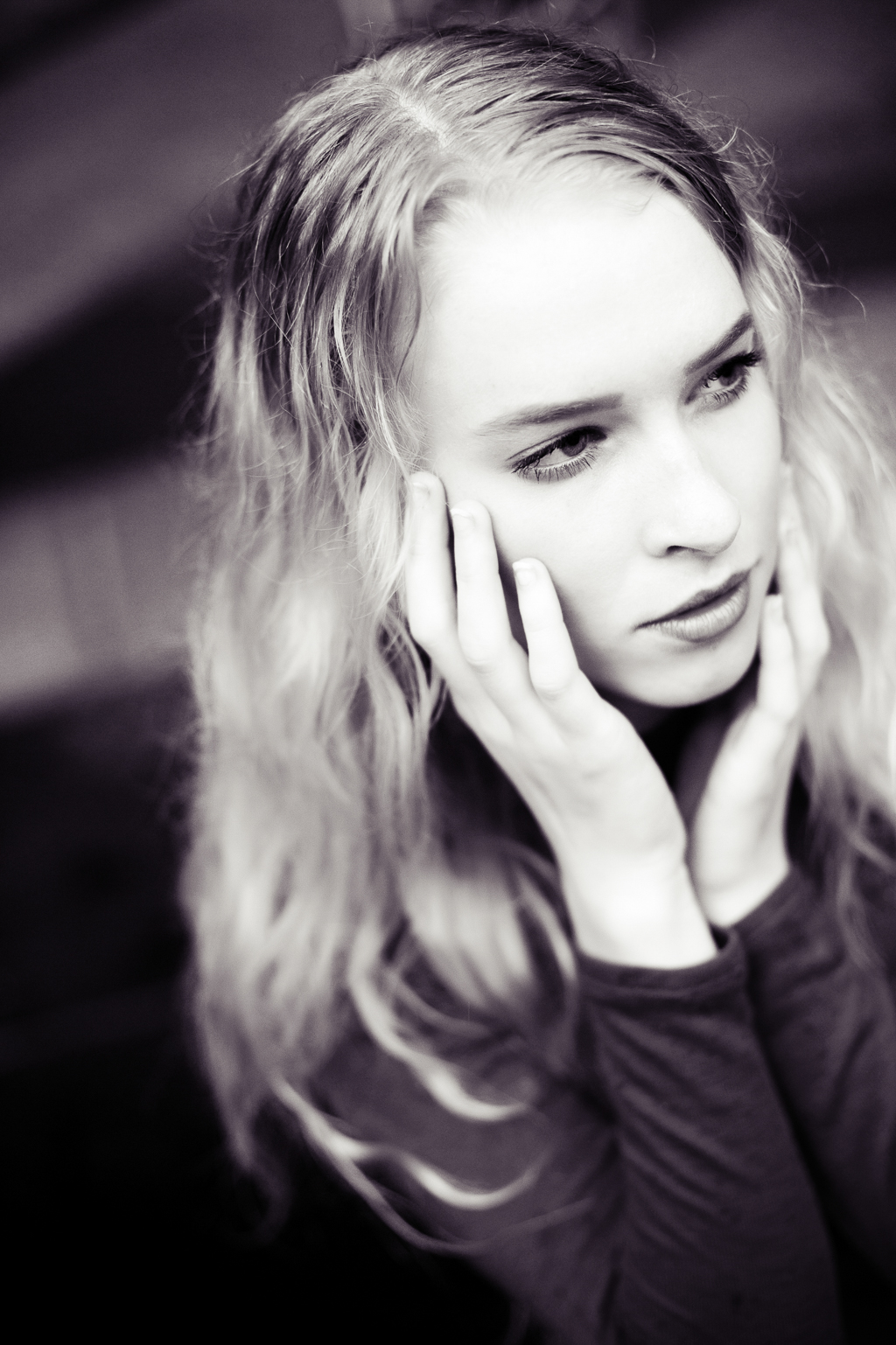 a black and white portrait of a model with long blonde hair holding her cheeks and looking away
