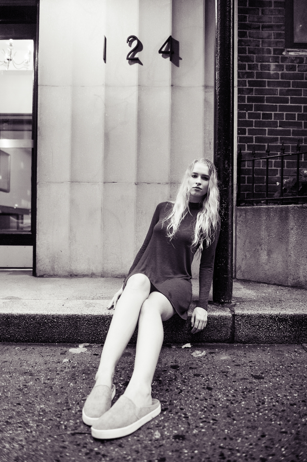 a black and white image of a model with long blonde hair sitting on a wet sidewalk 
