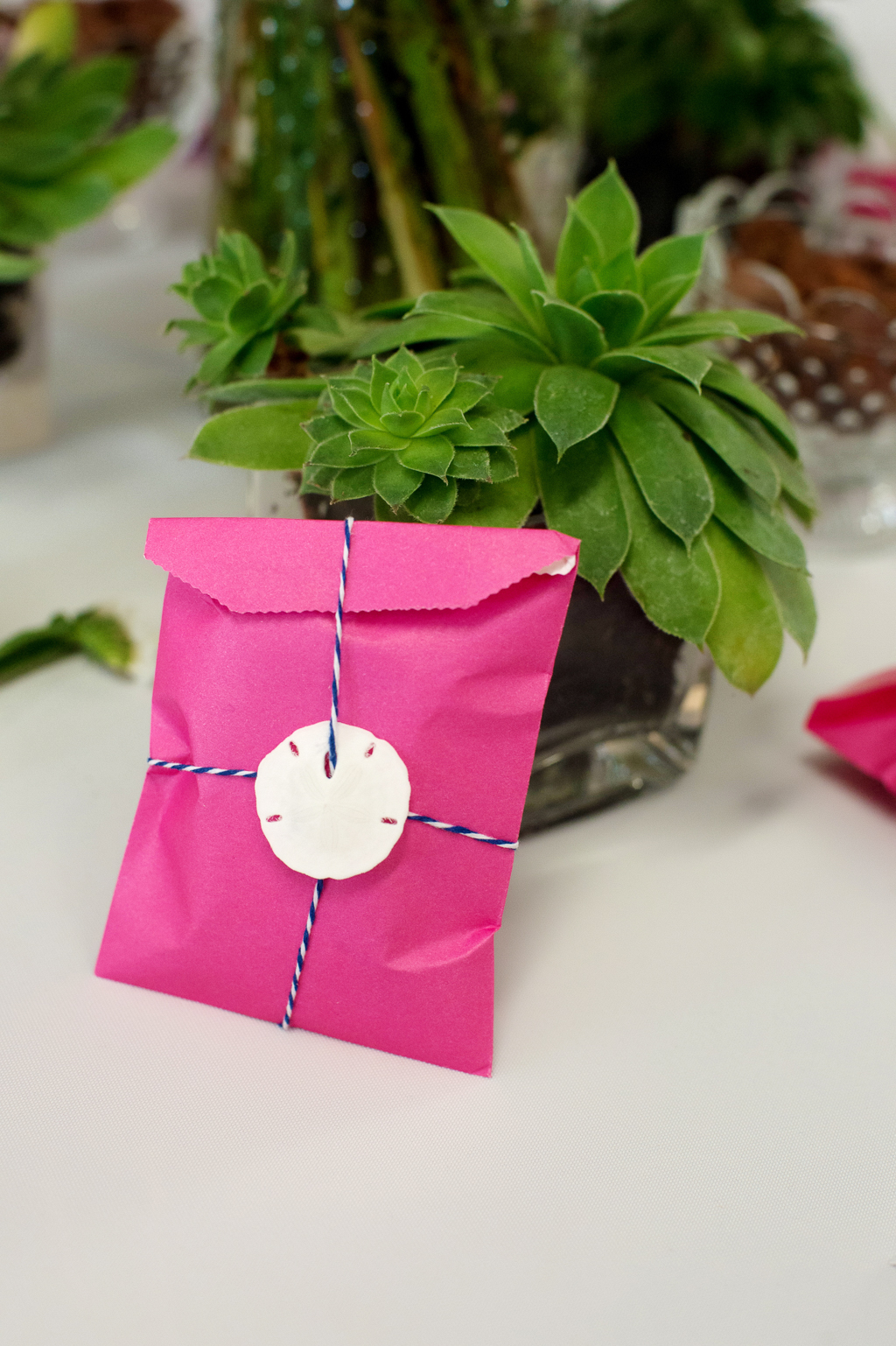 a sand dollar with bakers twine holds a gift bag closed as a wedding favor