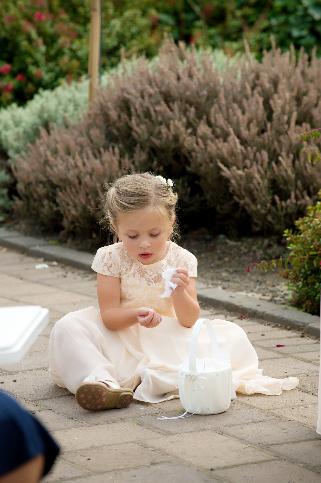 a flower girl sits on the ground playing with petals