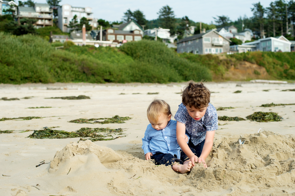 a little boy and a baby boy play in the sand on the beach