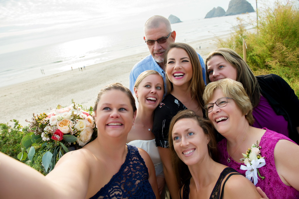 wedding guests huddle together for a selfie in front of the ocean