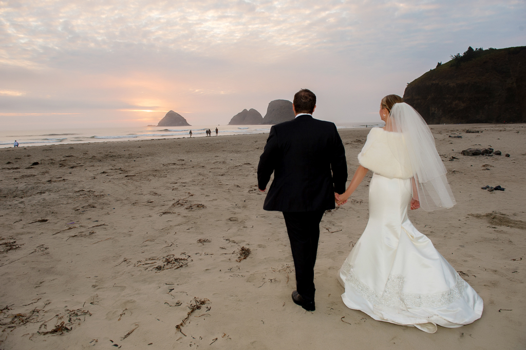 a bride and groom walk towards the ocean hand in hand at sunset