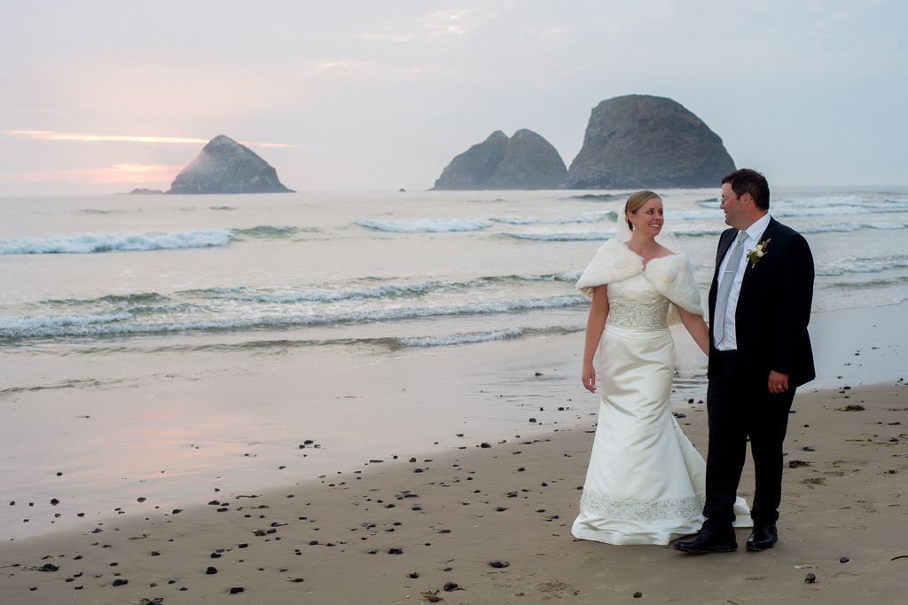 a bride and groom walk along the oregon coast at sunset