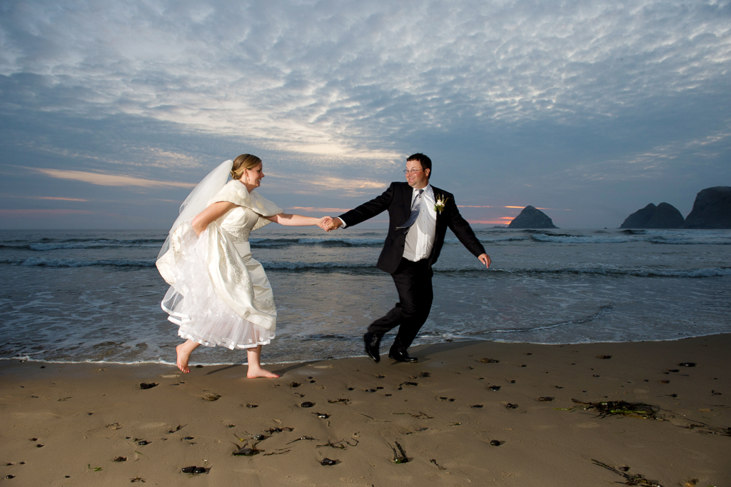 a groom playfully pulls his bride by the hand so she doesn't get wet by the ocean waves