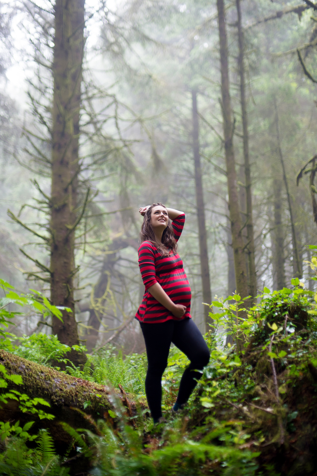 expecting mother stands on a moss and fern covered log in the foggy forest