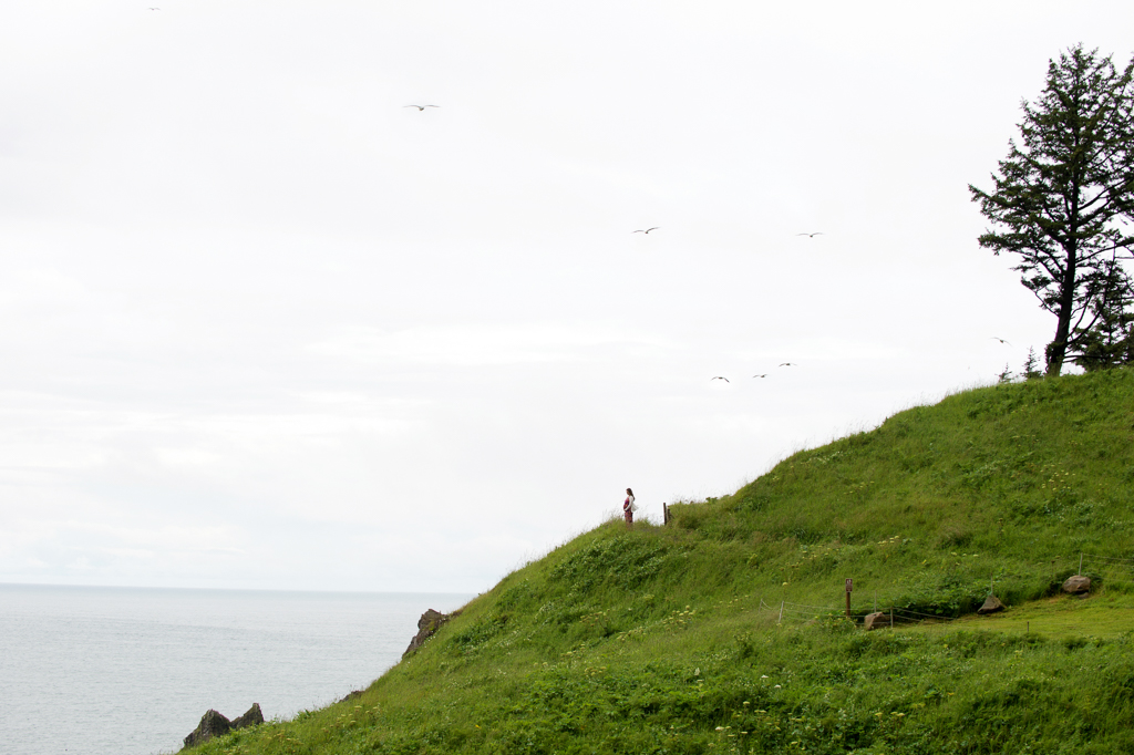 a pregnant woman stands in the far distance on a hill overlooking the ocean