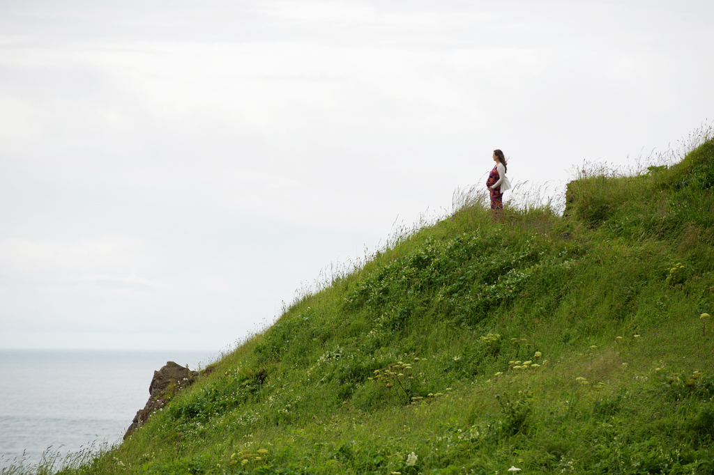 a pregnant woman stands at the top of a hill at ecola state park