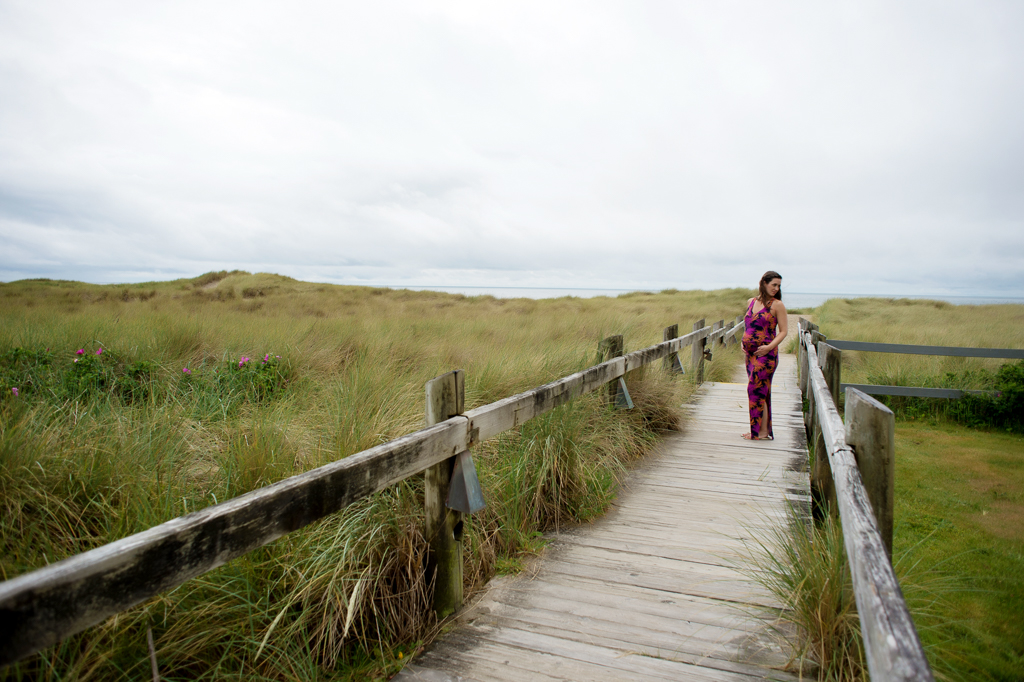 a pregnant woman stands on a long wooden walkway that leads to the pacific ocean