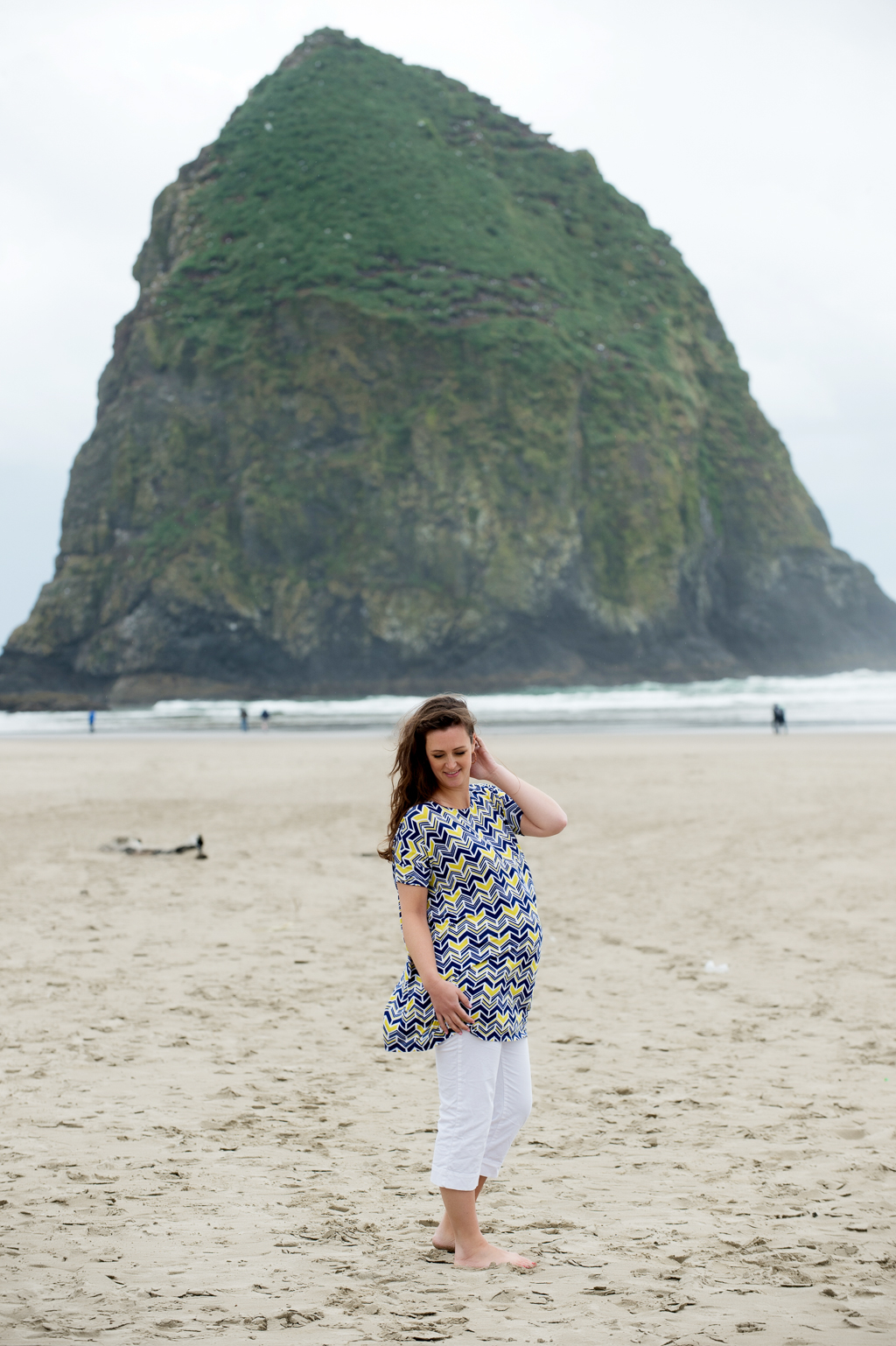 a pregnant woman stands in front of haystack rock at cannon beach