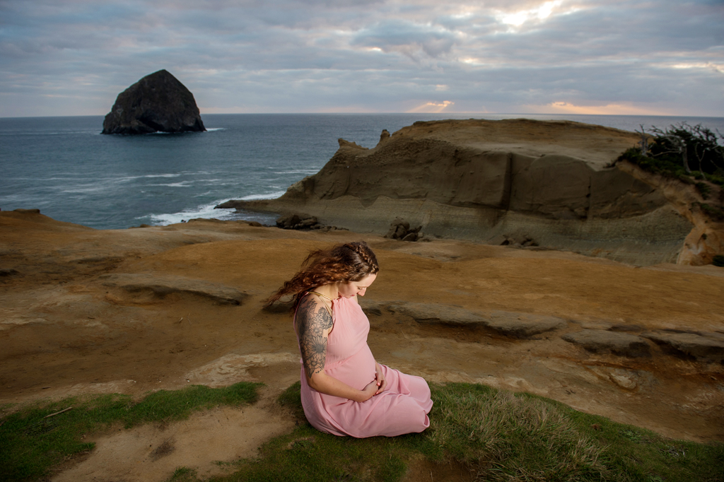 an expecting mother sits in the grass on the dunes that overlook pacific city ocean