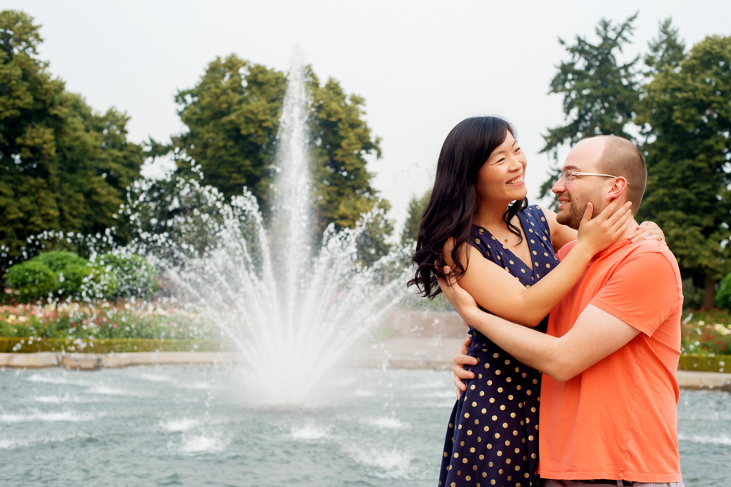 a couple hug each other in front of a water fountain