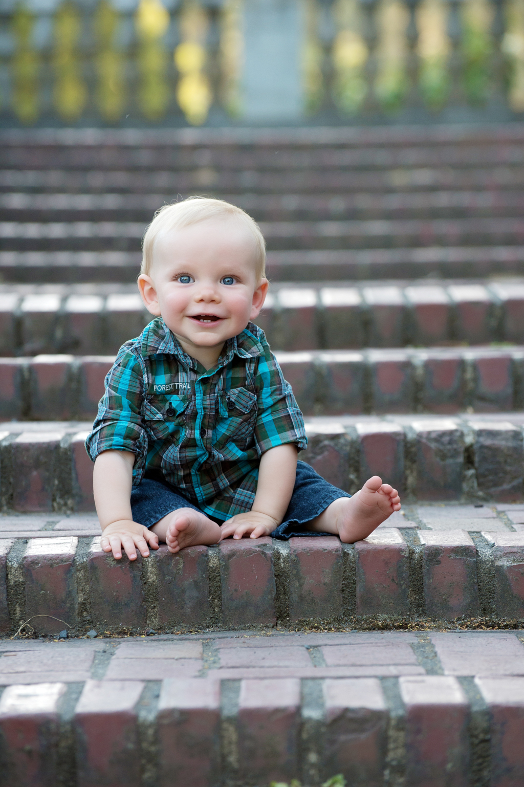 a baby boy with bright blue eyes sits on a brick step