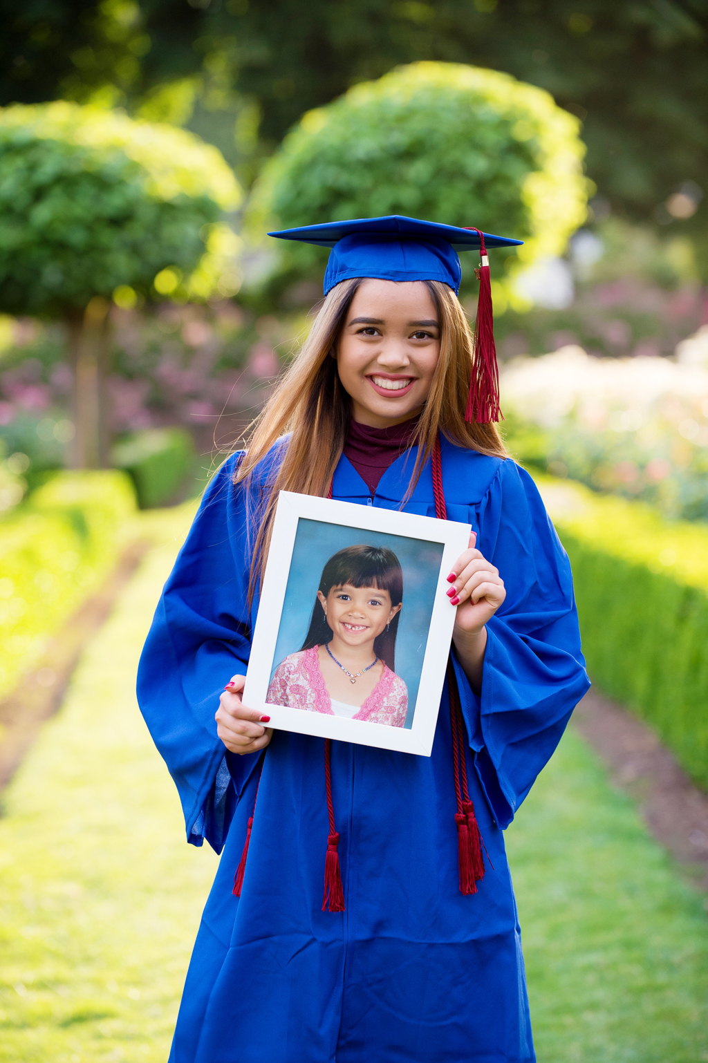a high school senior wears her cap and gown and holds a photo of herself in kindergarten