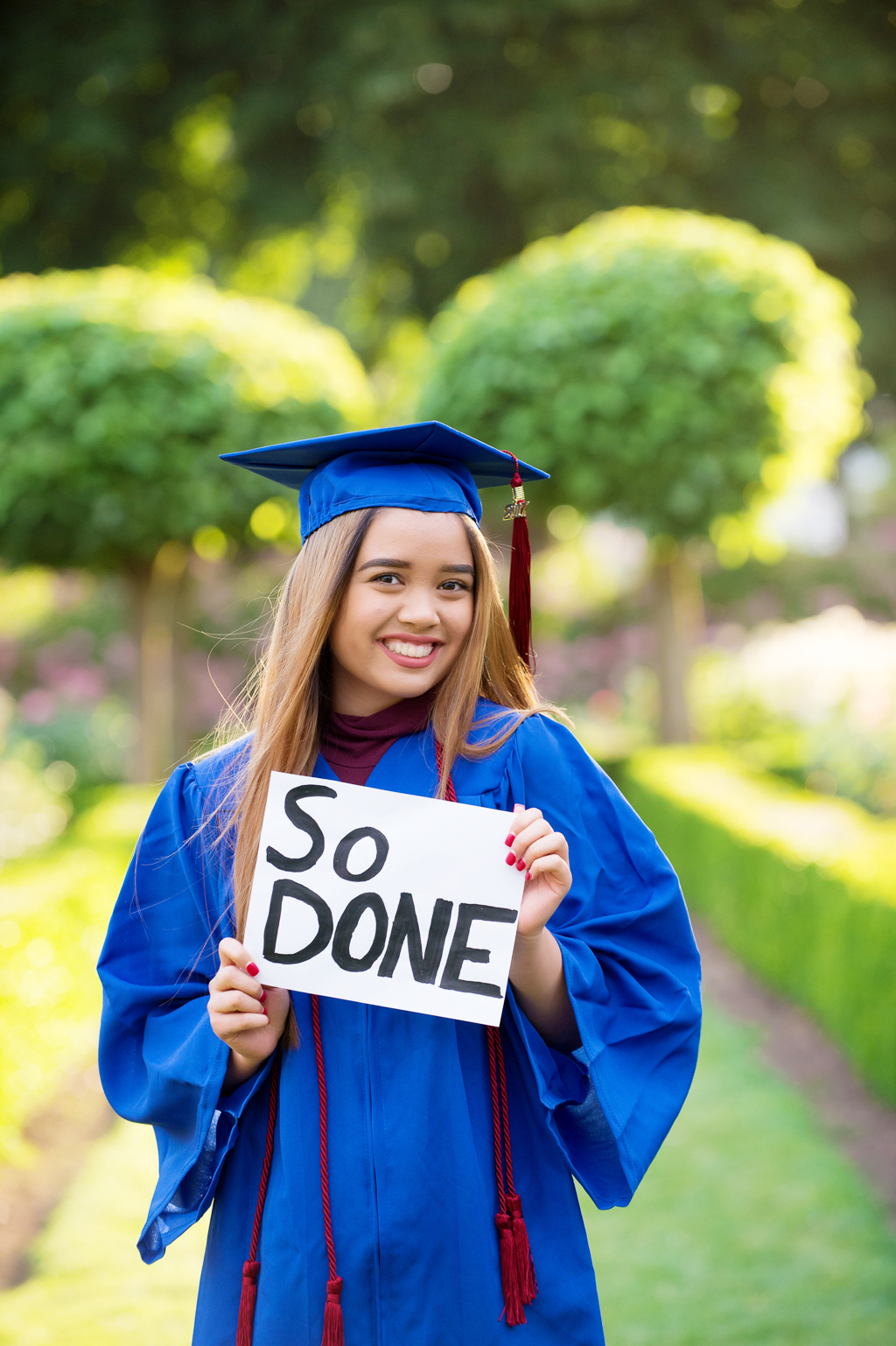 a high school senior wears her cap and gown and holds a sign that says So Done