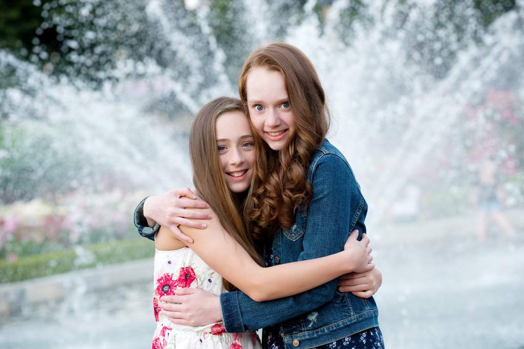 sisters embrace standing in front of the fountain at peninsula park