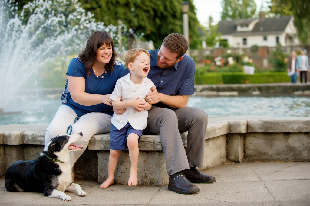 mom and dad tickles son while sitting on fountain at peninsula park rose garden