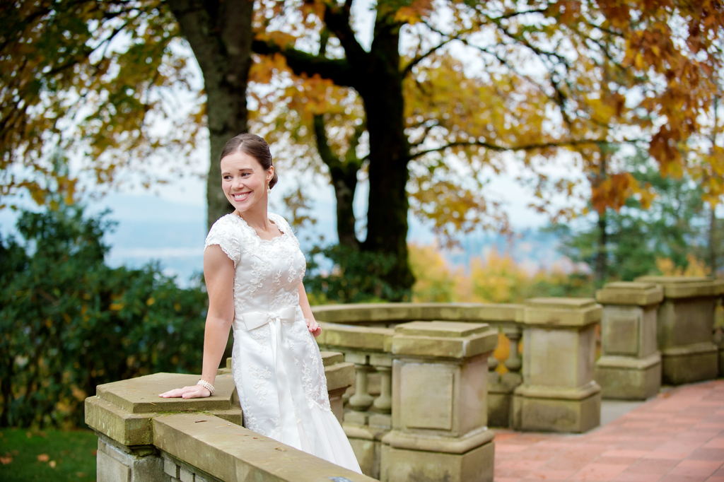 bride leans against porch at pittock mansion with autumn colors surrounding her