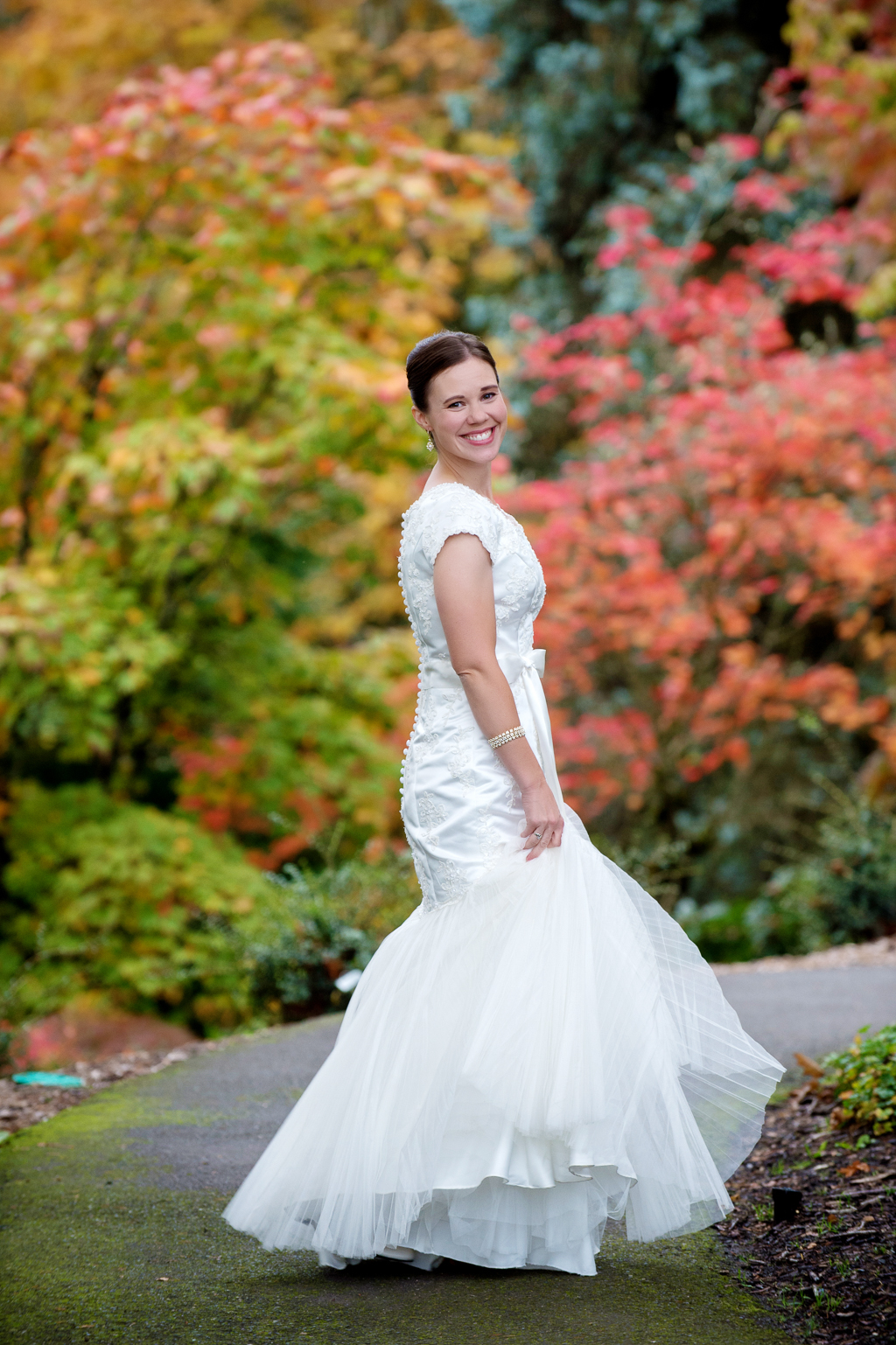 bride spins around on walking path surrounded by orange and red autumn leaves