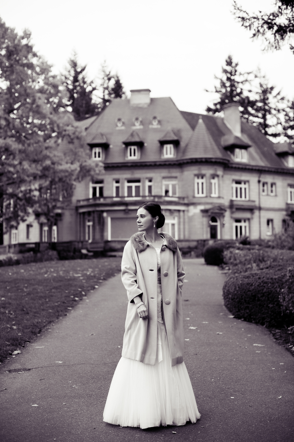 black and white portrait of a bride wearing a fur collared coat in front of pittock mansion