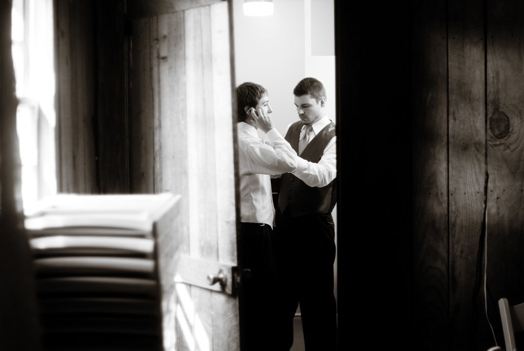 best man helps groom put on tie while groom is on phone
