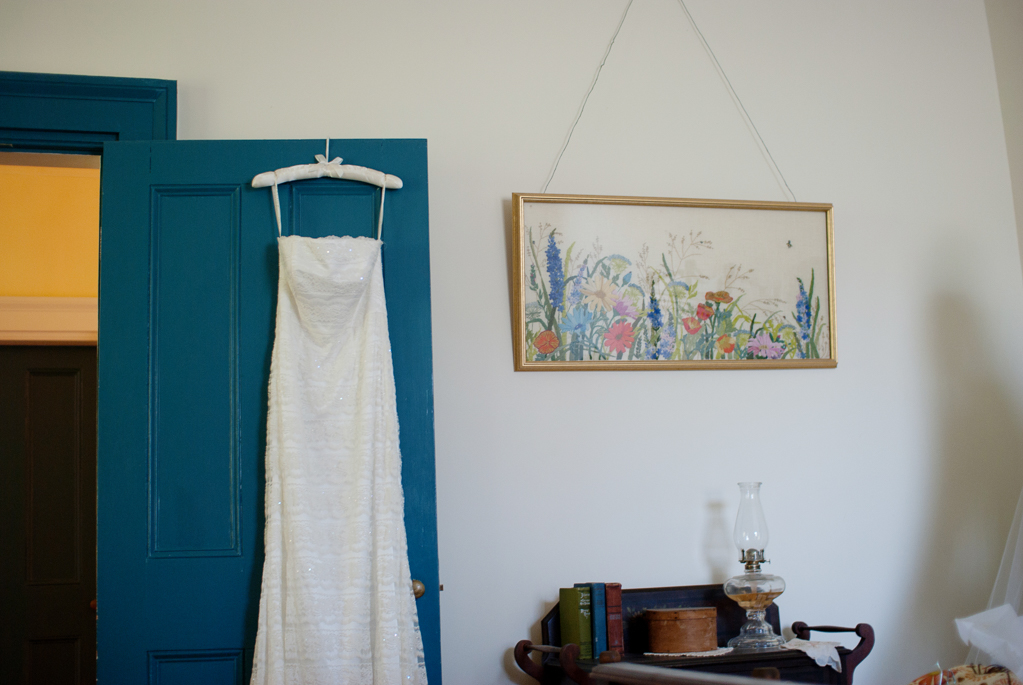 wedding dress hangs on turquoise door next to colorful wildflower painting