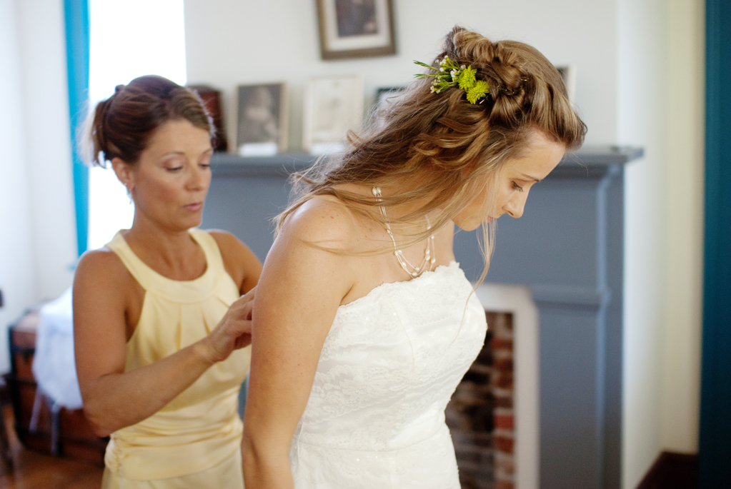 mother helps bride into wedding dress