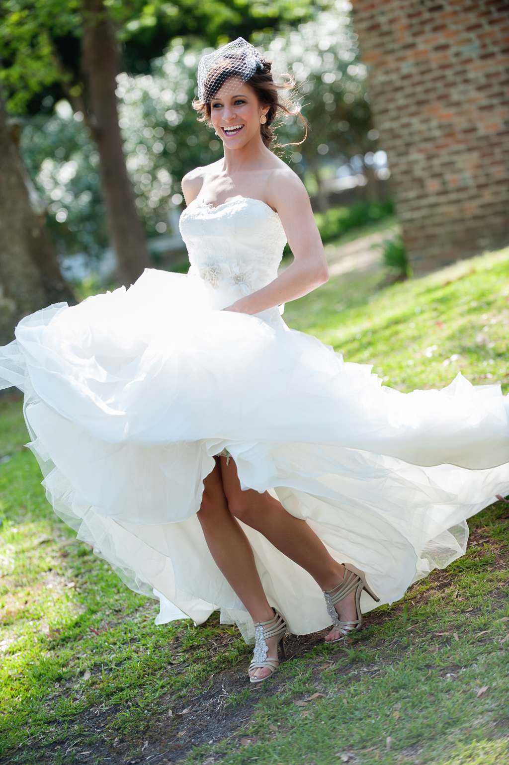 bride swings up wedding dress excitedly as she dances in yard