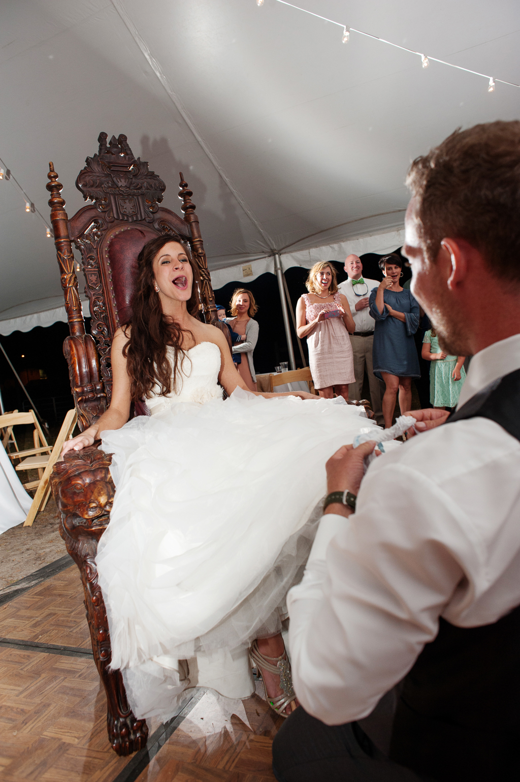 bride sits in a gigantic antique plantation chair and screams as groom goes for her garter