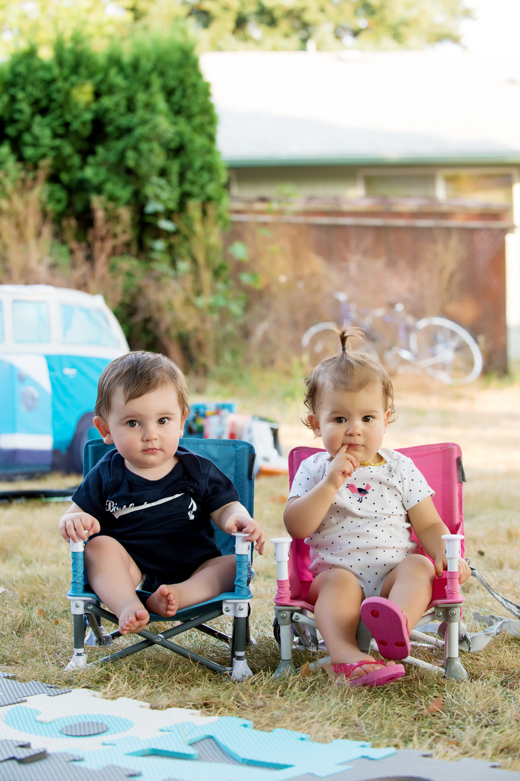 a baby girl and boy sit side by side in miniature pink and blue camping chairs