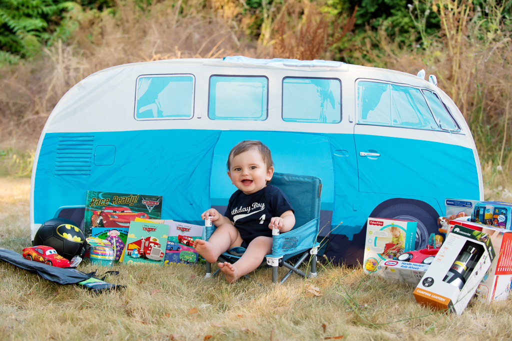 a baby boy sits in a camp chair in front of a tent that looks like a vw bus van