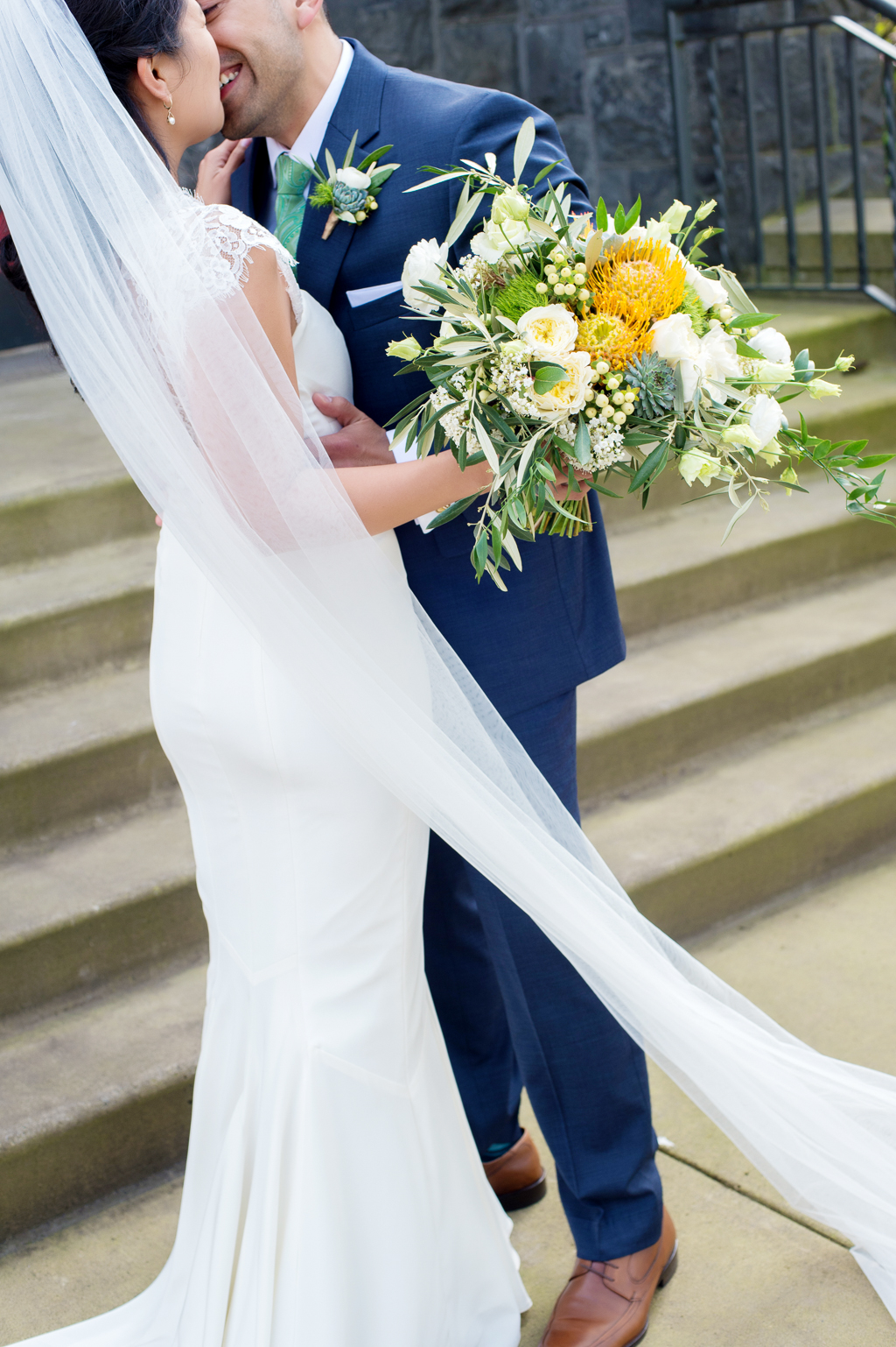 bride with very long wedding veil holds vibrant yellow and white bouquet