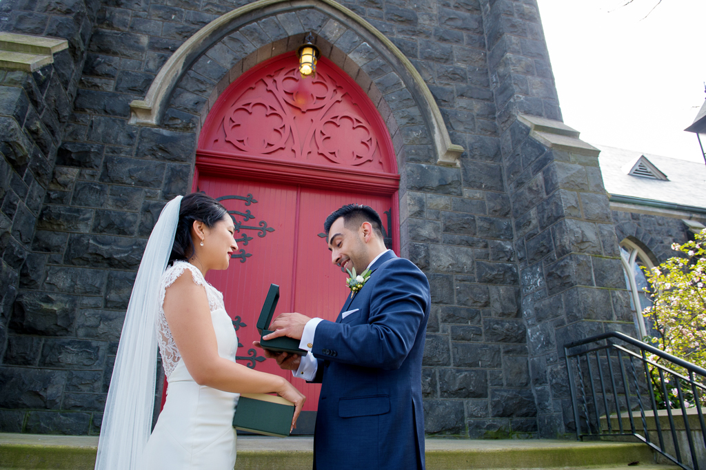 bride gives groom a wedding gift in front of a church with a red door