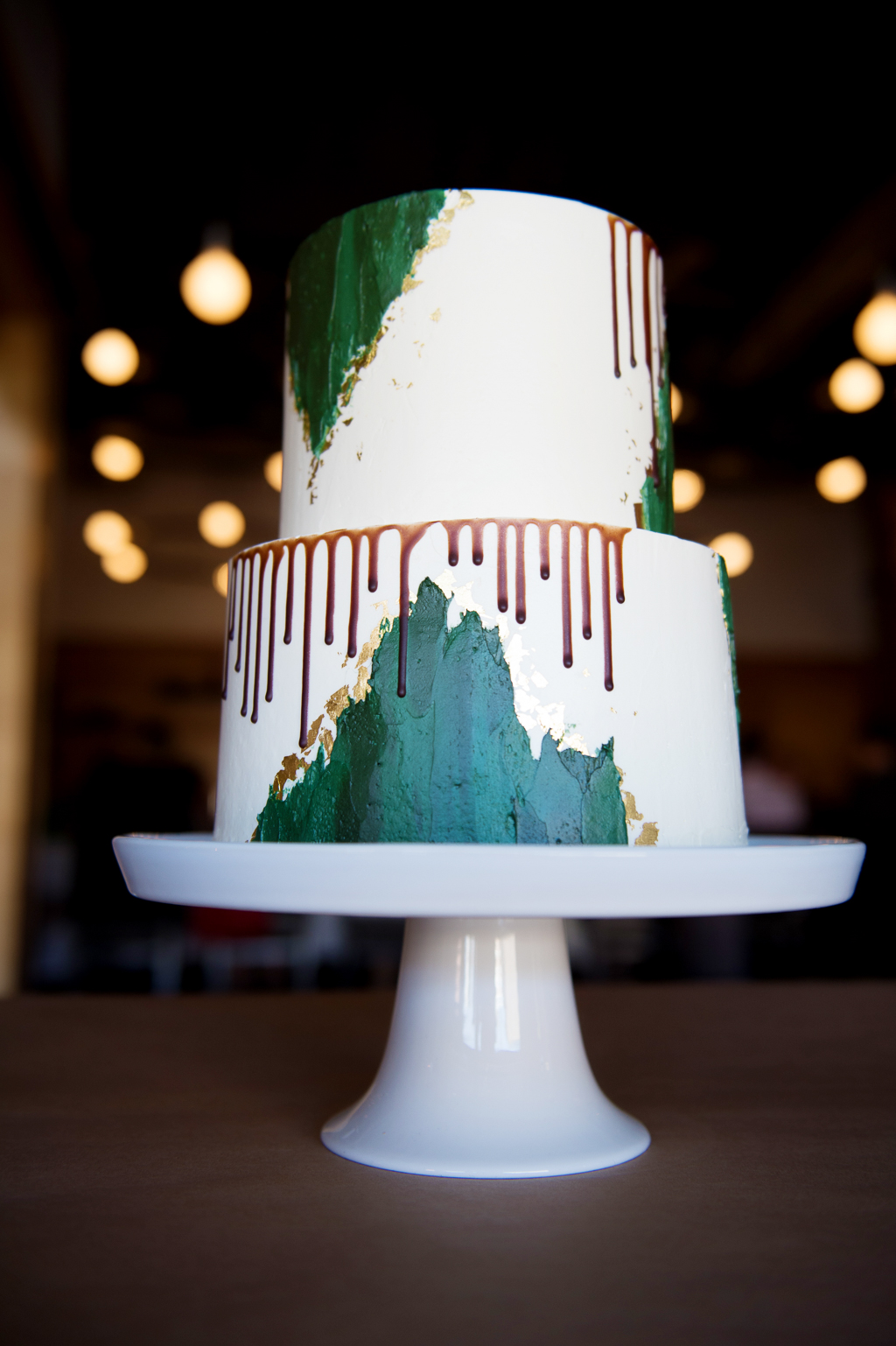 a white wedding cake with green and gold and dripping chocolate