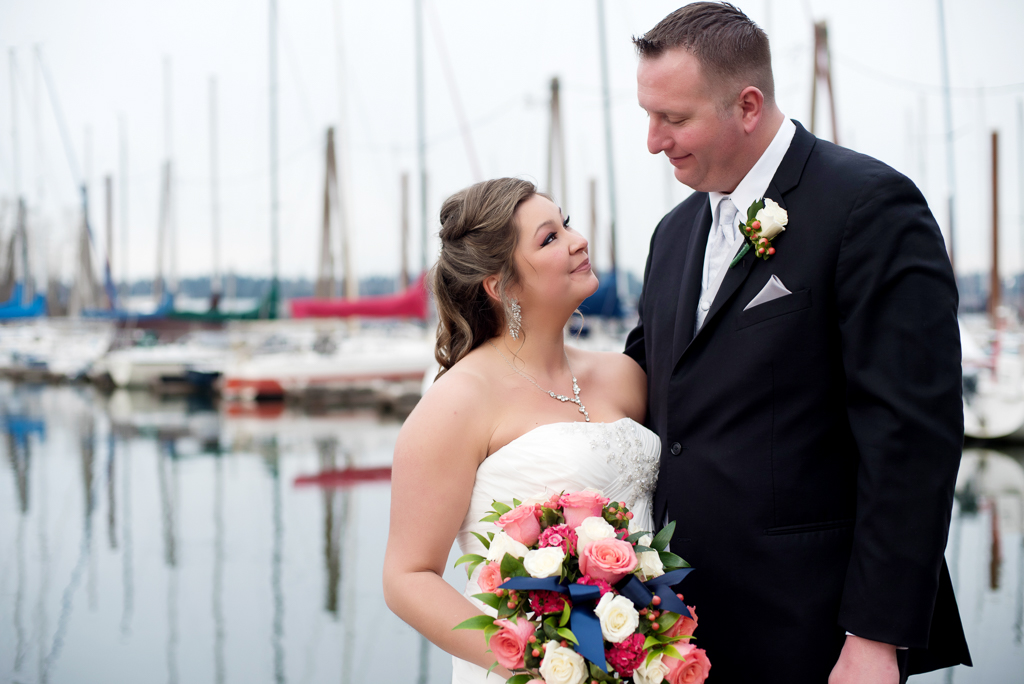 bride and groom look at each other in front of sailboats