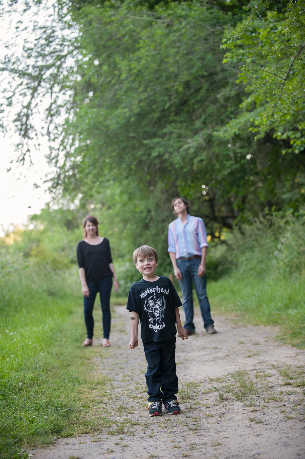 young boy wears motorhead t-shirt and stands in front of parents on a dirt trail