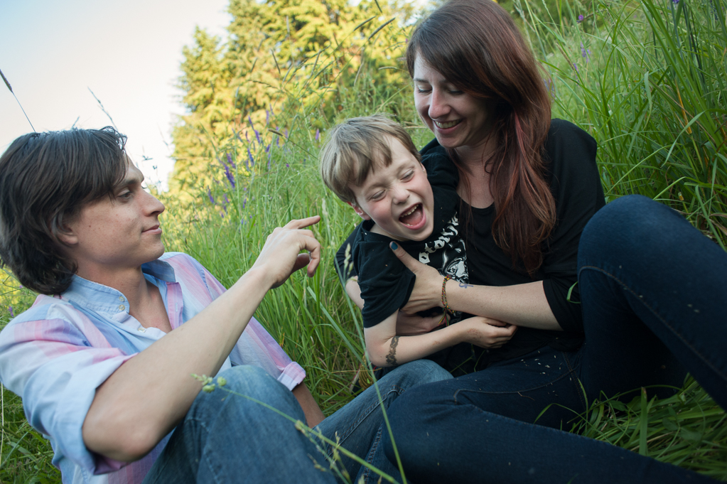 parents tickle a little boy wearing a motorhead tshirt while sitting in tall grass