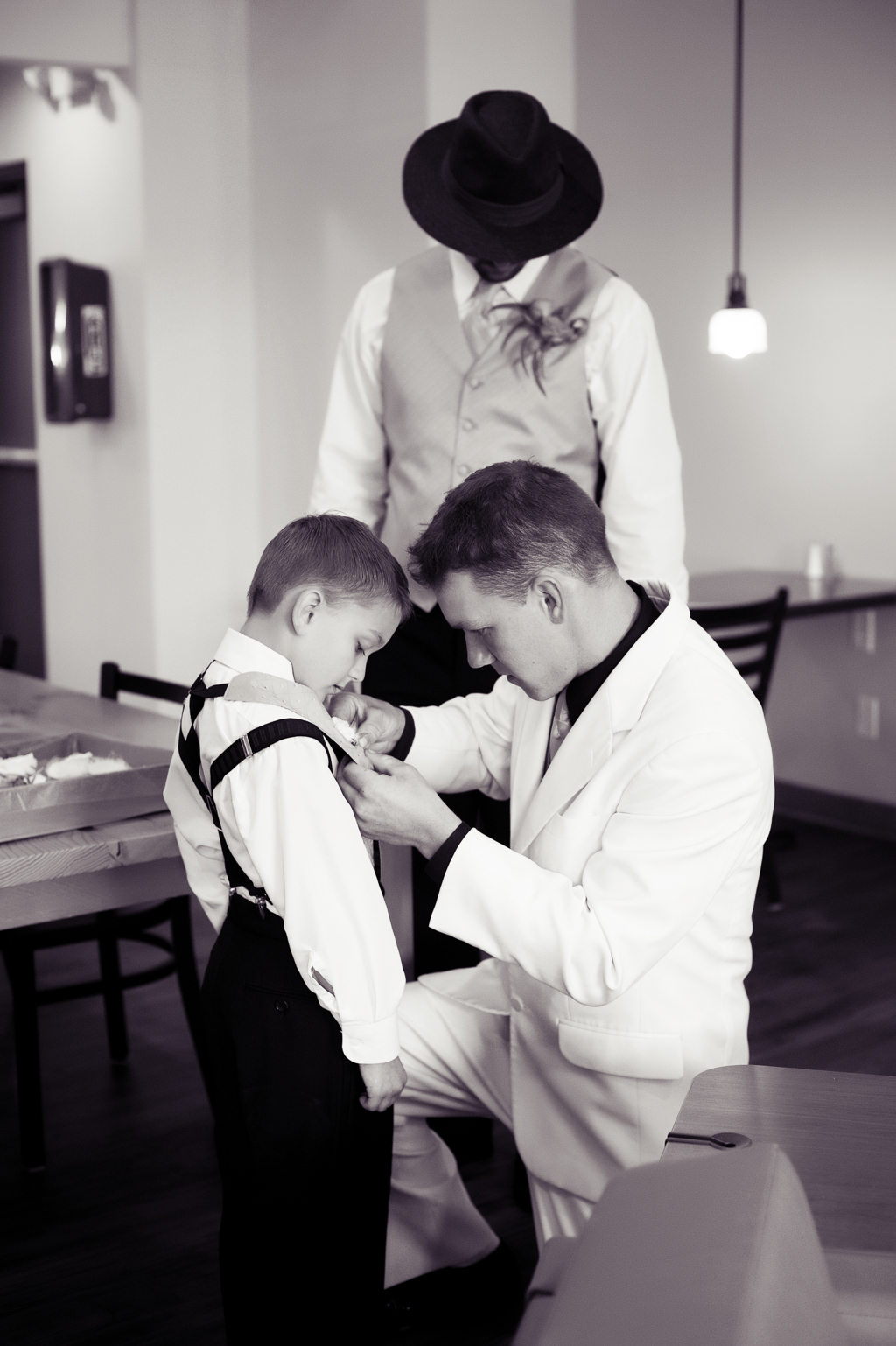groom helps young boy with suspenders