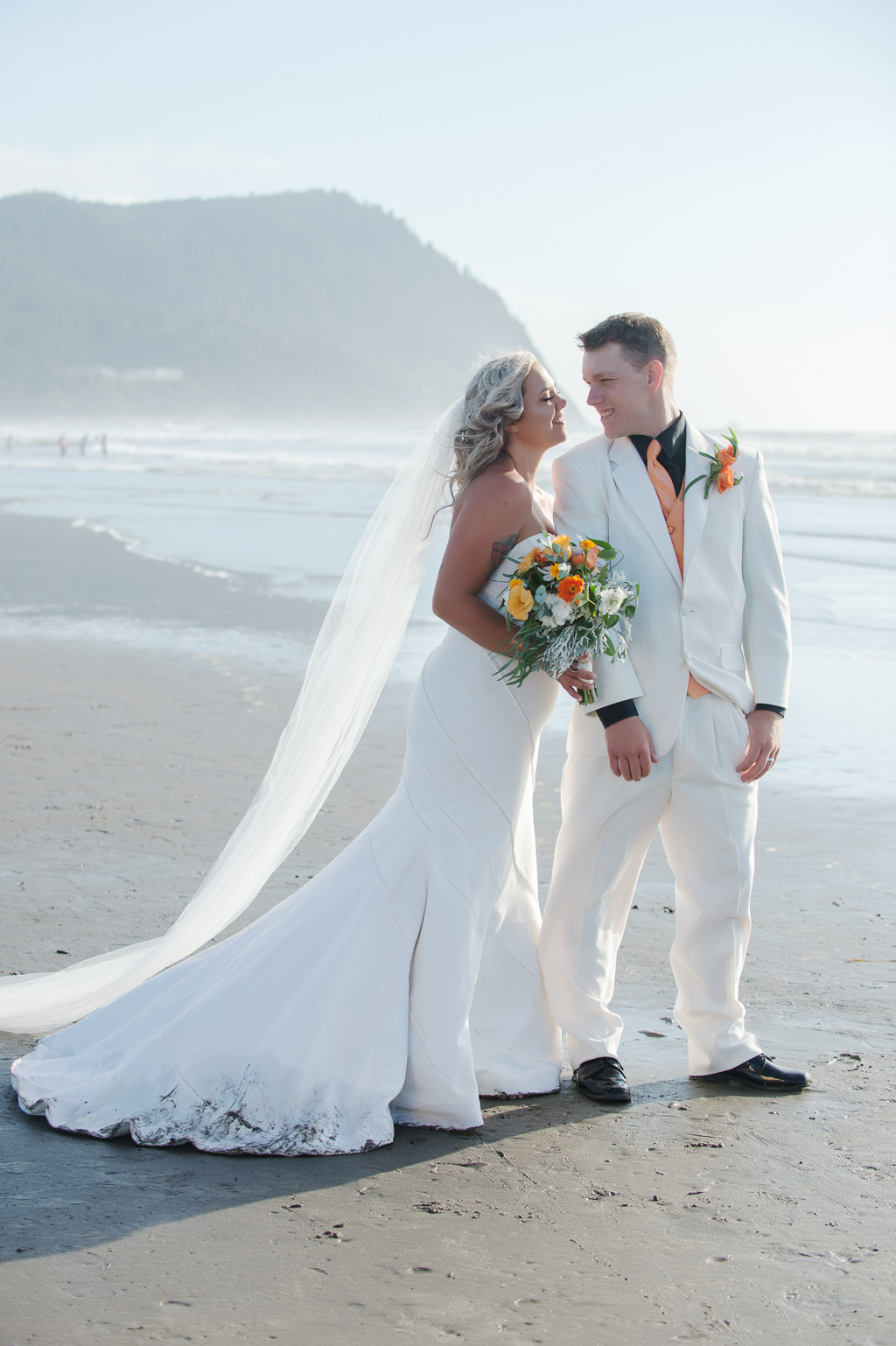 bride and groom hug on seaside beach with orange and yellow bouquet