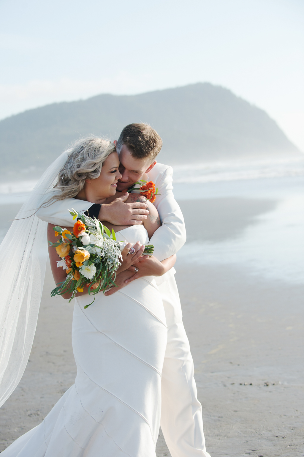 bride and groom hug on seaside beach with orange and yellow bouquet