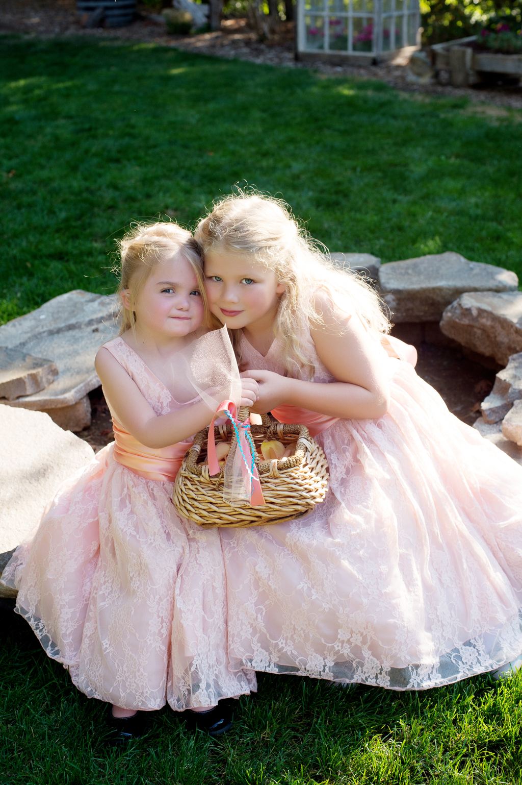flower girls in pink dresses hold a basket and hug together