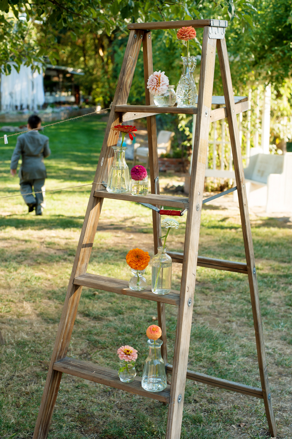 an old ladder holds vases of zinnias for wedding decor