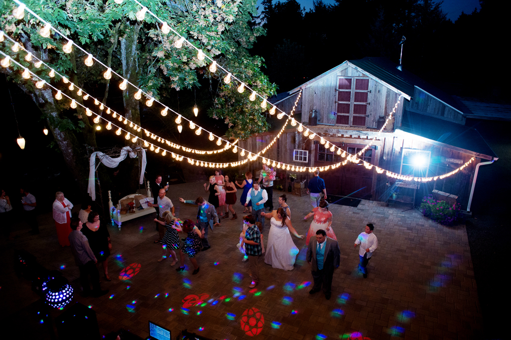 cafe lights hang above the dance floor outside the barn at a wedding reception