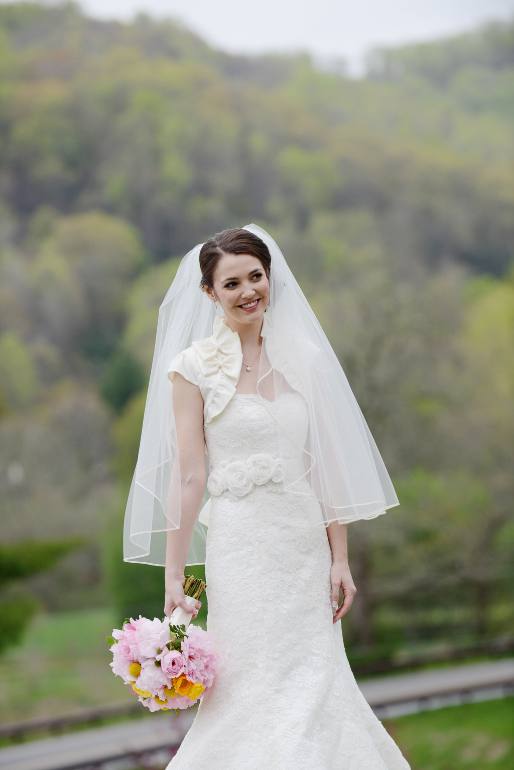 a bride holding a pink and yellow bouquet stands in front of the blue ridge mountains