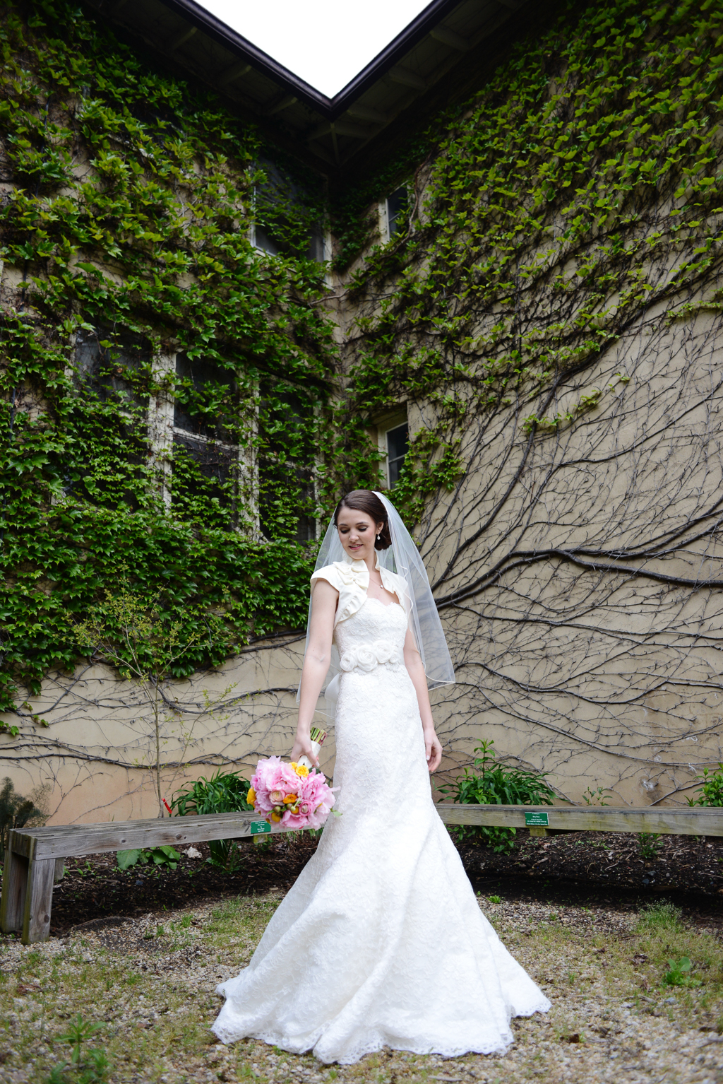 a bride holds a pink and yellow bouquet in front of an ivy and vine covered wall