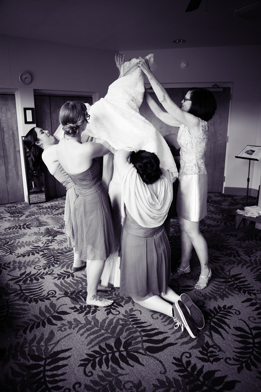 bridesmaids and her mother help a bride into her wedding dress