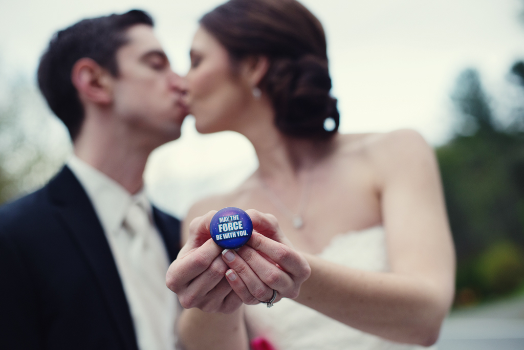 a bride and groom kiss as they hold out a pin that says may the fourth be with you a reference to star wars and their wedding date