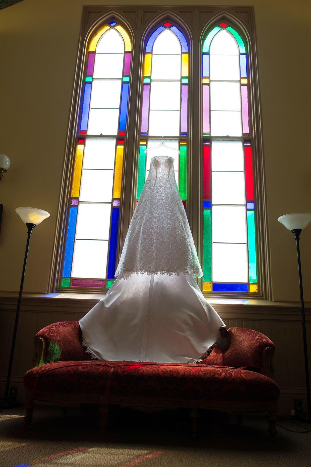 a wedding dress hangs from a large stained glass window